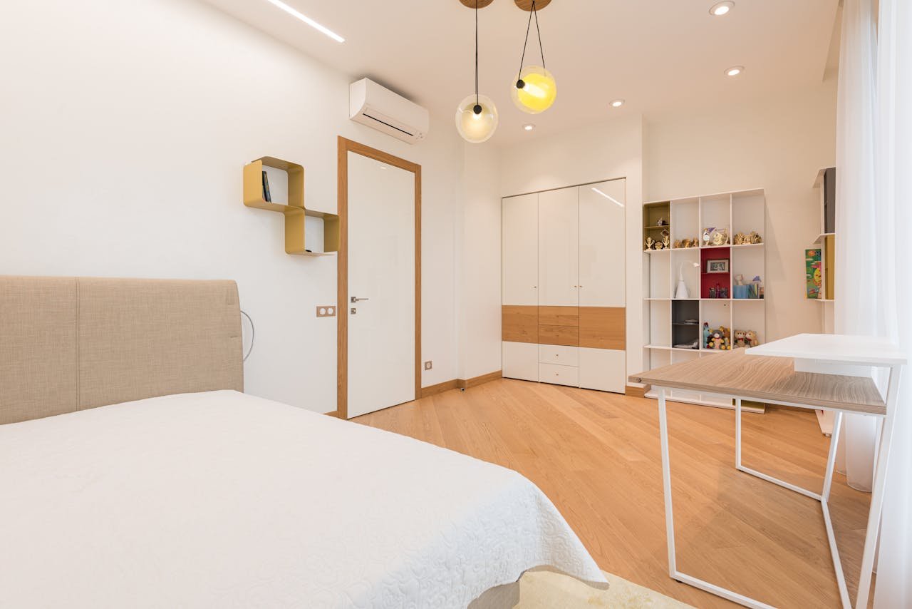 Comfortable bed with wooden table placed in in contemporary bedroom with wardrobe and shelves with various decorative items